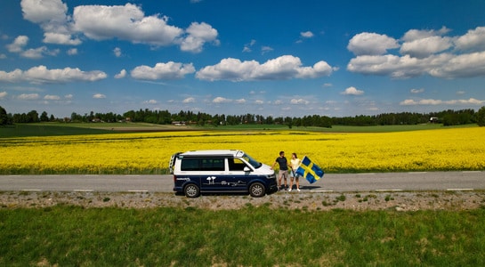 campervan standing on a road with 2 people holding a Sweden flag