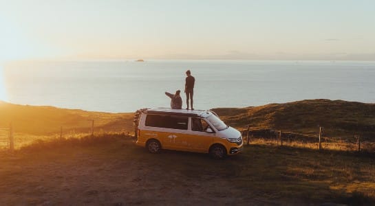 A couple standing on a VW camper looking into the sunset