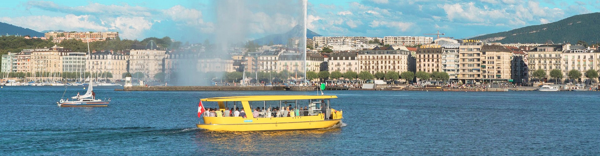 Yellow water taxi driving over lake Geneva with fountains and the city visible in the background.