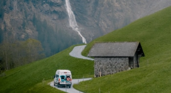 roadsurfer campervan driving on a road in Switzerland with a waterfall in the backgrounds comming out from the mountain