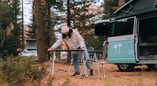 Woman putting up picnic table next to a campervan in the forest