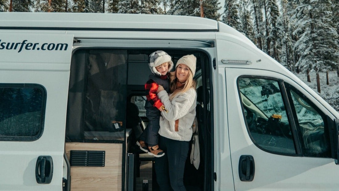 Woman holding a child in front of a white camper during winter