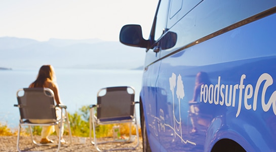 woman in a chair next to a lake and a campervan in summer