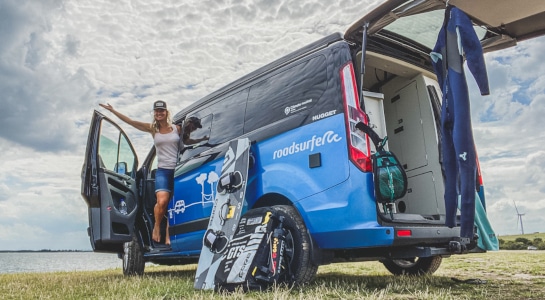 woman in the door of a blue campervan with a wakeboard next to it