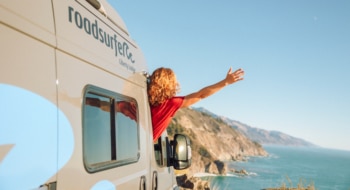 Woman leaning out of camper overlooking the sea.