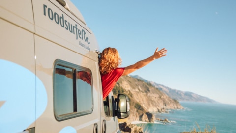 Woman leaning out of camper overlooking the sea.