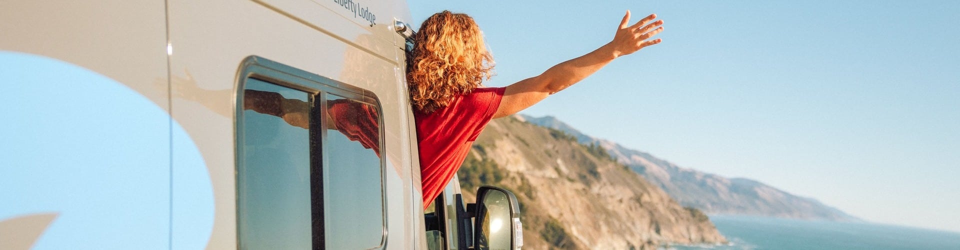 Woman leaning out of camper, overlooking the sea.