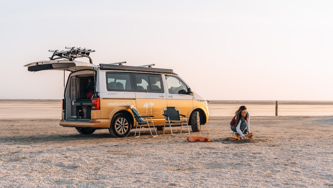 woman making fire next to a camper van on a beach