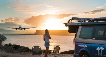 Woman standing next to campervan overlooking the sea and a plane starting during sunset.