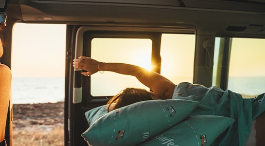 Woman laying in bed leaning forward to open up the door of her camper.