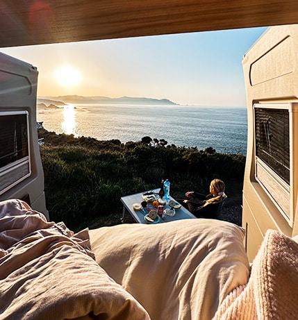 Woman sitting at breakfast camping table seen from inside of the campervan.