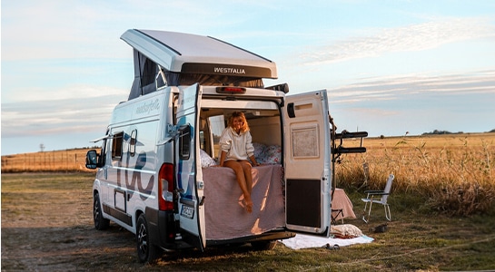 woman sitting in a camper van next to a field in summer