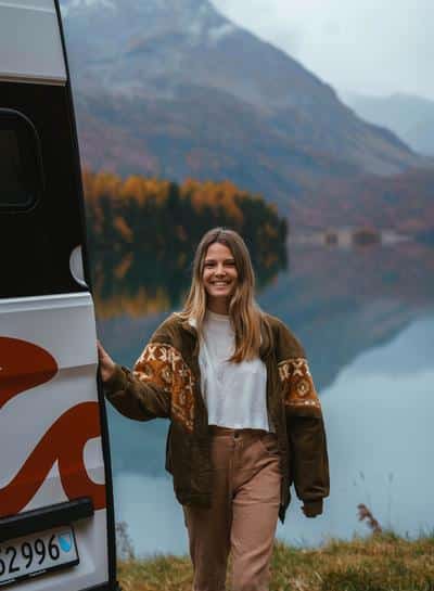 Woman standing beside an RV in the mountains, representing the experience of RV rentals near me