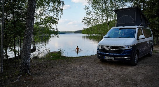 woman taking a dip in a lake next to a camper van