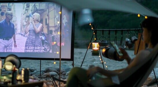 Woman sitting on a camping chair watching a movie on an outdoor cinema screen.