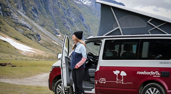 woman with hat looking up a mountain in the door of a camper van