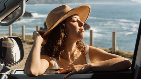 Woman wearing a sunhat leaning on campervan window while enjoying the sun.