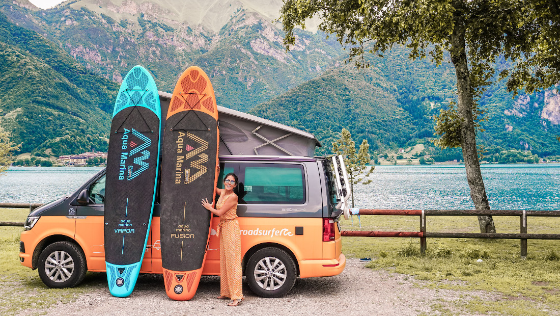 woman with two sup boards in front of a campervan