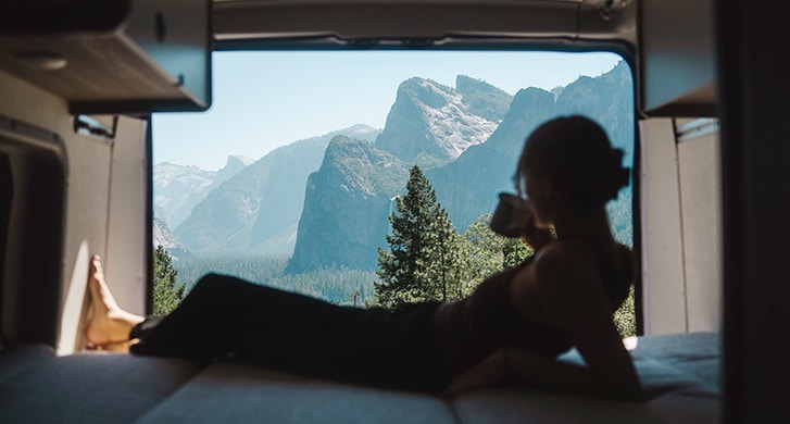 Women Drinking Coffee And Looking Out Campervan At Mountains