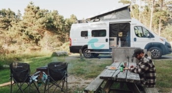 Man eating at a picnic table beside his camper van in a wooded campsite, capturing the relaxed experience of camping near San Francisco at Marin Park