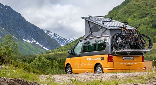 yellow camper van with pop up roof and bike rack in nature