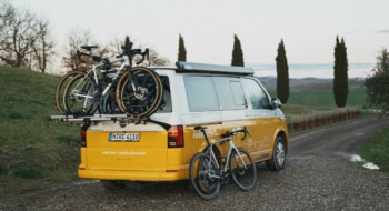 yellow campervan with three bikes in a landscape in Tuskany