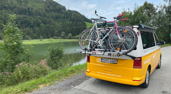 Yellow roadsurfer campervan with a bike rack next to a river