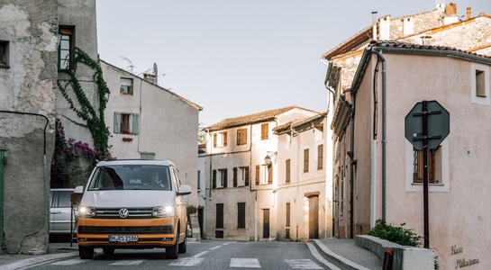 Yellow VW campervan from roadsurfer cruising through a town