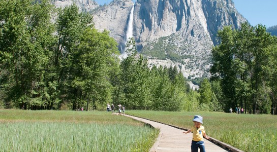 Child on a wooden boardwalk in Yosemite Valley with waterfall and granite cliffs—things to do in Northern California with kids.