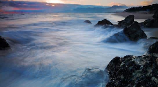 Waves crashing against rocks at sunset along Zuma Beach in Malibu, California