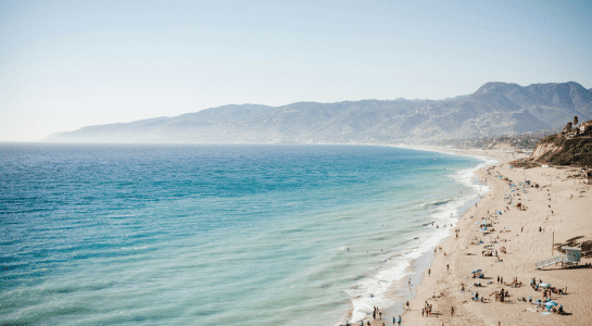 A long stretch of sandy shoreline with mountains in the distance and clear blue water, highlighting the best beaches in Los Angeles